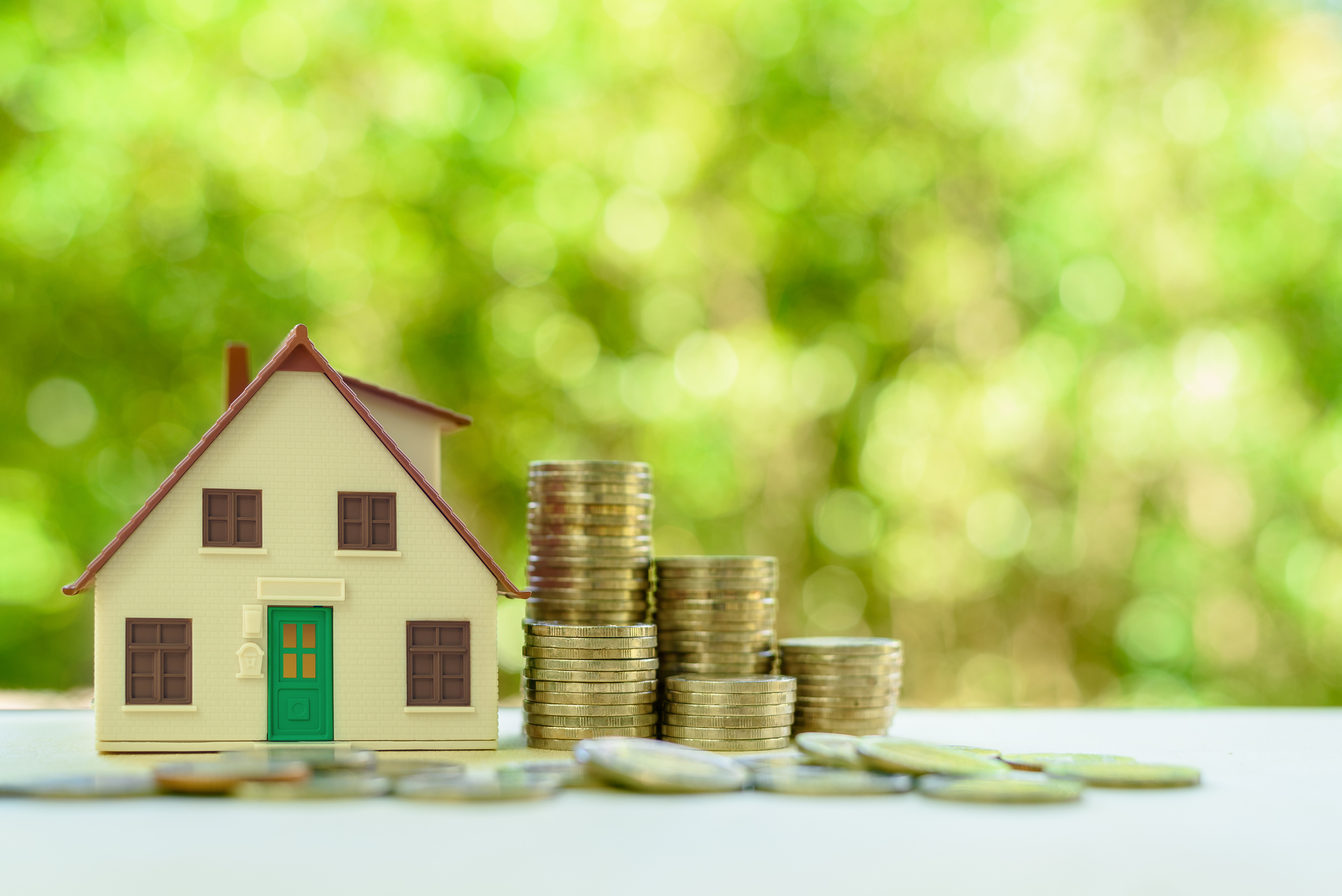 Property investment / reverse mortgage, financial concept : Small home or house model with green door and stacks of rising coins, depicts saving money to buy a new residential asset, human basic needs